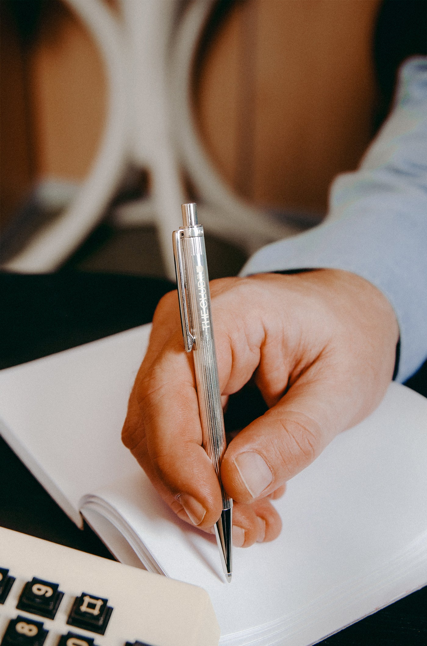Close-up of a hand writing with a silver metallic pen on a notebook.

