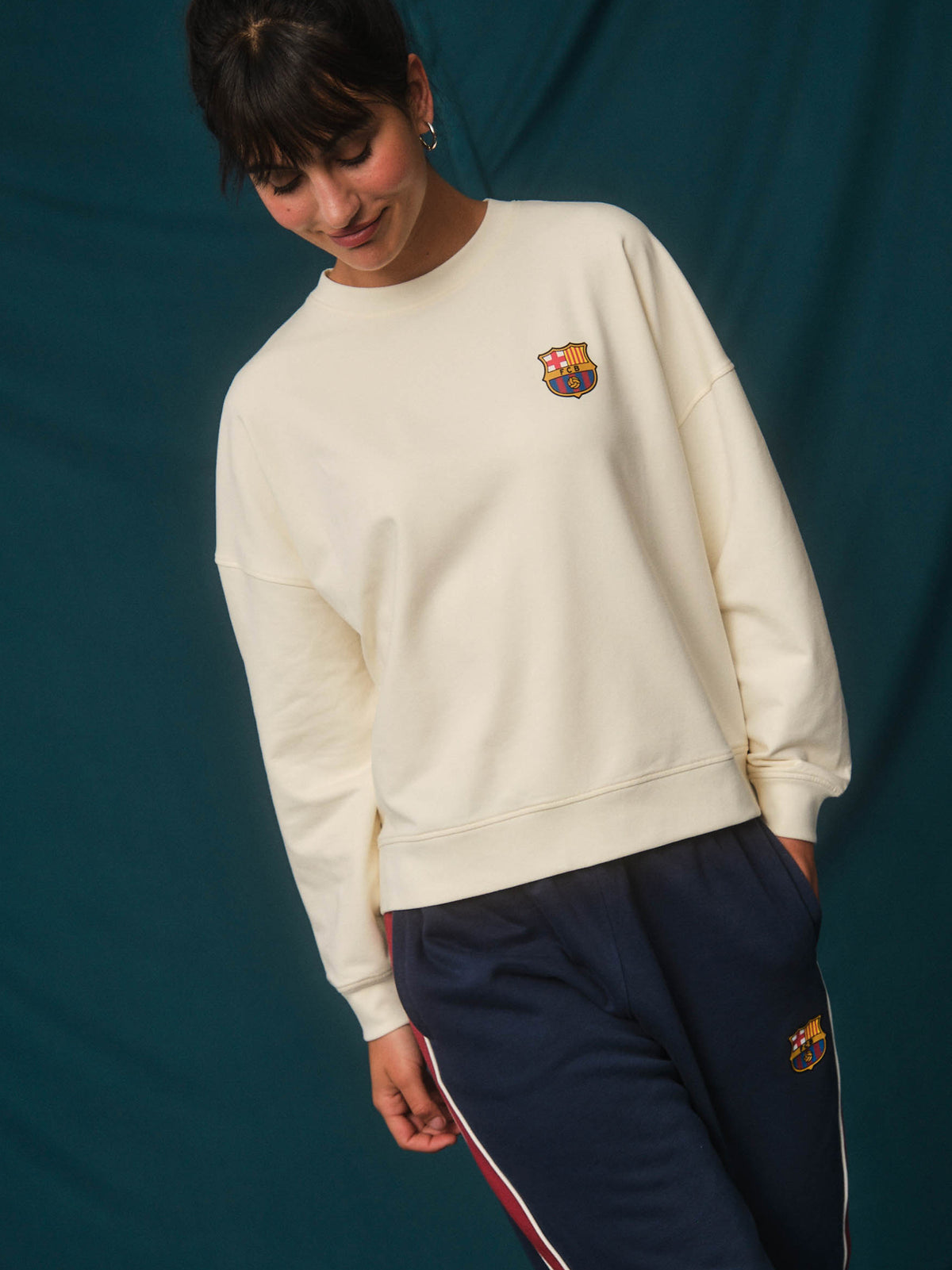 Model wearing an off-white FC Barcelona sweatshirt with a small crest on the chest and navy Barça track pants with side stripes.