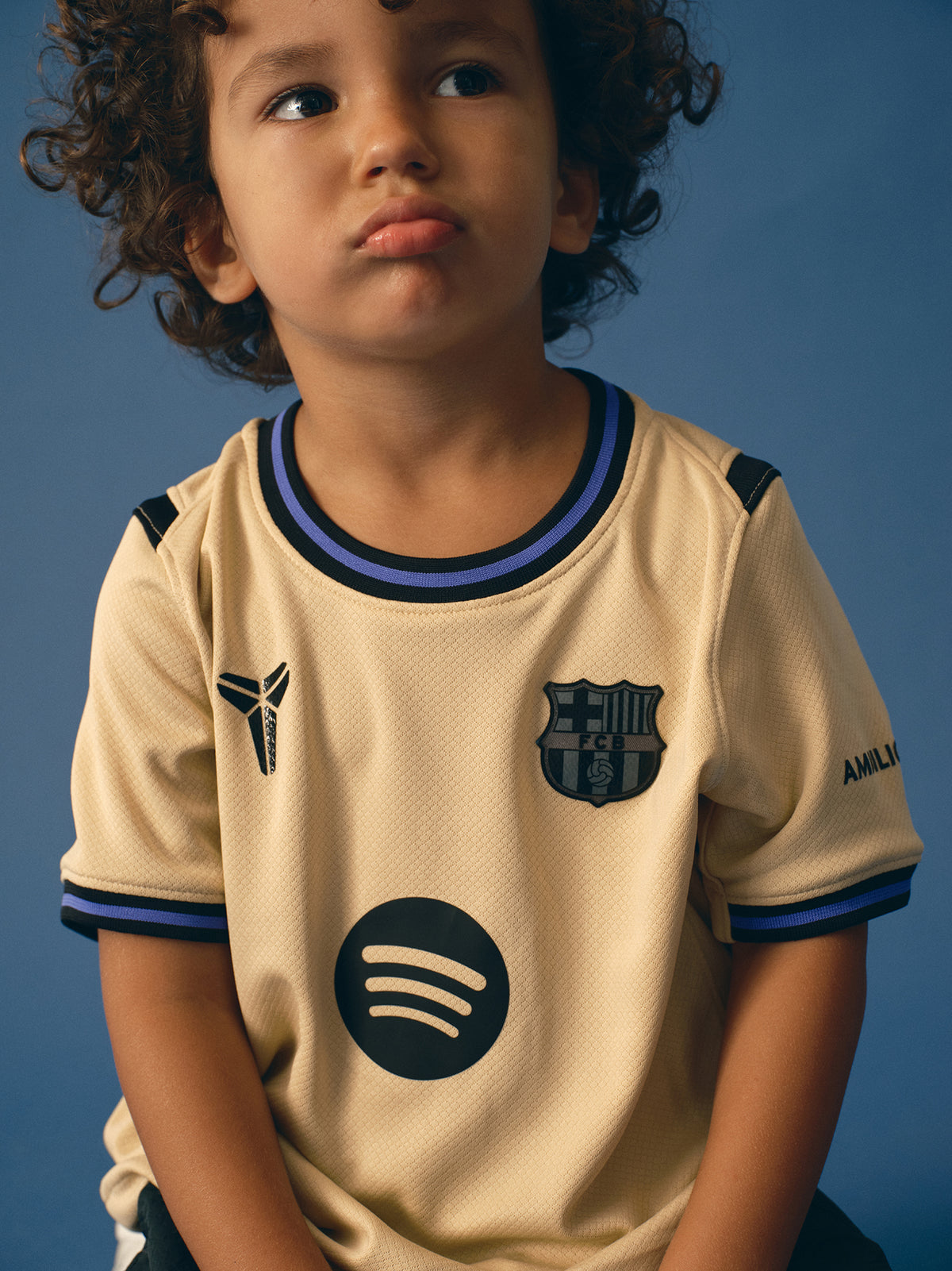 FC Barcelona kids' away kit set including beige jersey with black and purple details, black shorts with purple accents, and matching black socks, featuring club crest, Nike logo, Spotify sponsor, and Kobe Bryant tribute emblem.