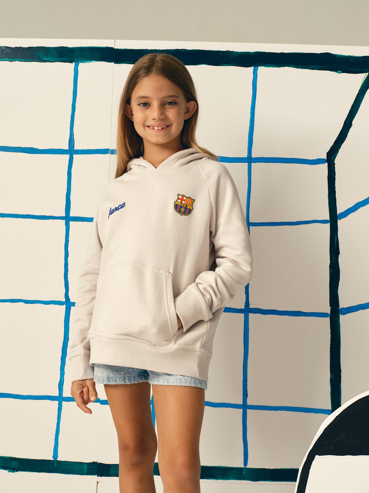 White FC Barcelona hoodie featuring a unique back design with a four-petal flower made of circular emblems: the St. George cross, Catalan flag, blaugrana stripes, and a central golden football. Below the graphic, the text reads “Futbol Club Barcelona” and “Més que un club” along with minimalist logos.