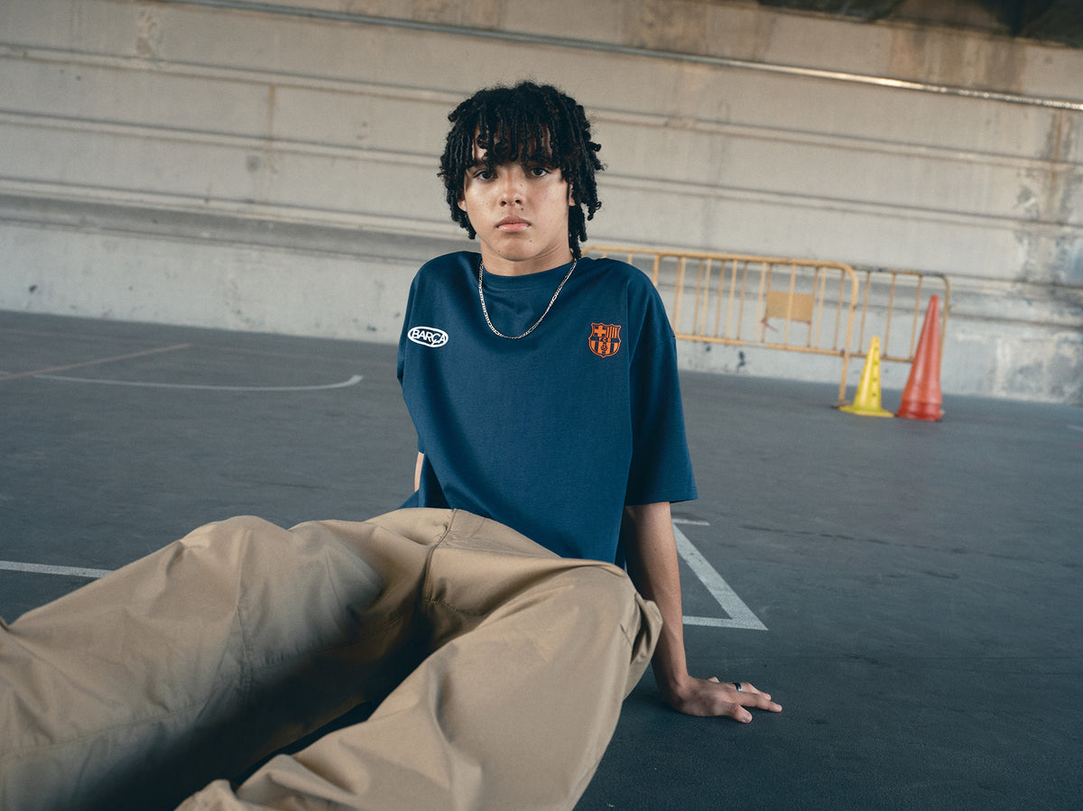 navy blue FC Barcelona t-shirt with the text 'CULERS OF THE WORLD' in orange and a white line illustration of a footballer kicking a ball.