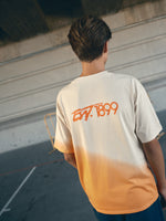 beige and orange gradient FC Barcelona t-shirt with 'EST. 1899' printed in bold orange text.