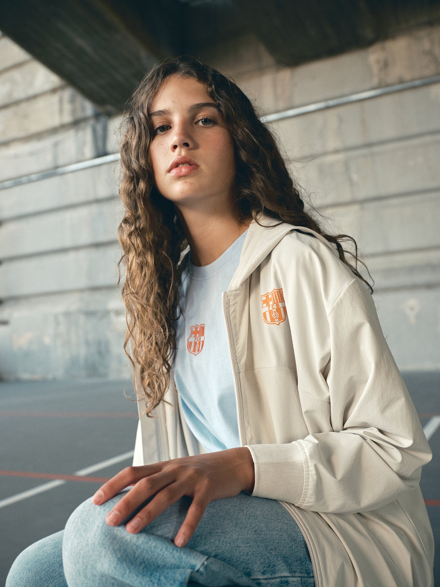 Beige FC Barcelona hooded jacket with minimalist orange graphic icons and text printed across the upper back.