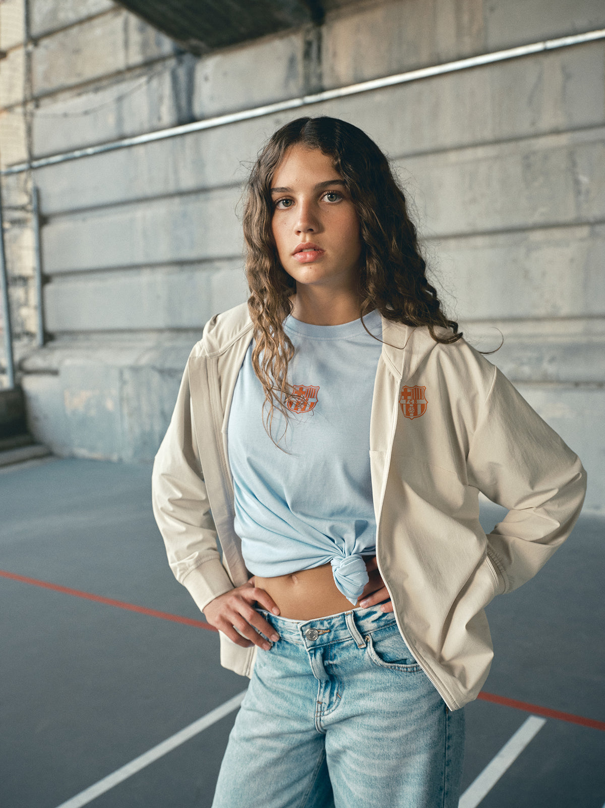 Beige FC Barcelona hooded jacket with minimalist orange graphic icons and text printed across the upper back.