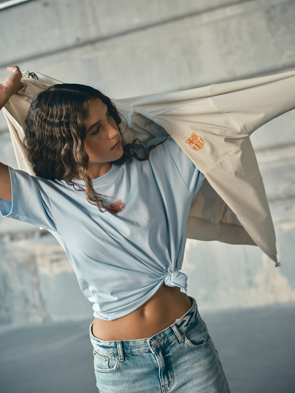 Beige FC Barcelona hooded jacket with minimalist orange graphic icons and text printed across the upper back.