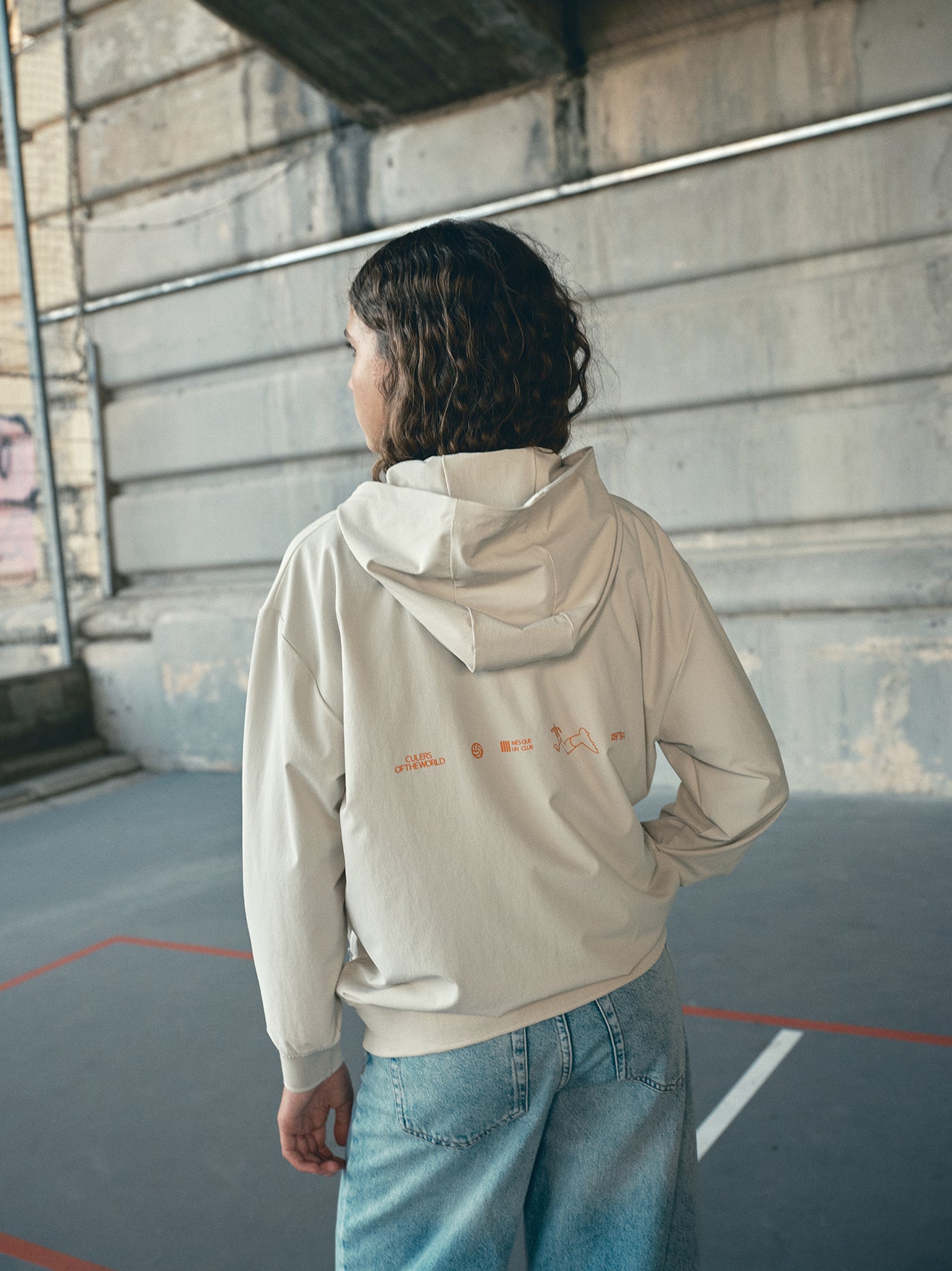 Beige FC Barcelona hooded jacket with minimalist orange graphic icons and text printed across the upper back.