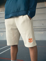 beige FC Barcelona shorts featuring the club crest in orange on the left leg