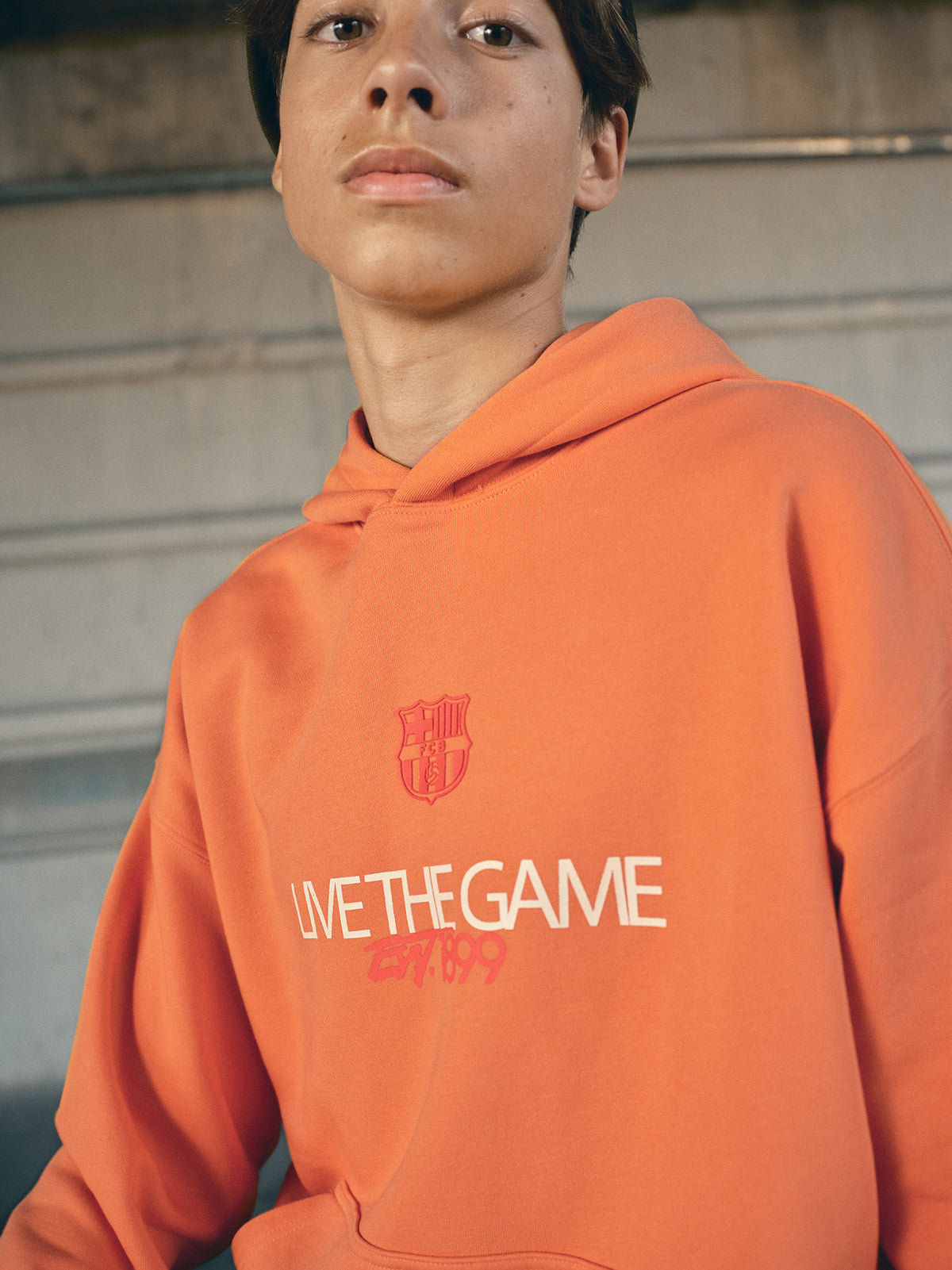 Orange FC Barcelona hoodie featuring the club crest and the slogan 'Live the Game EST. 1899' printed on the front.