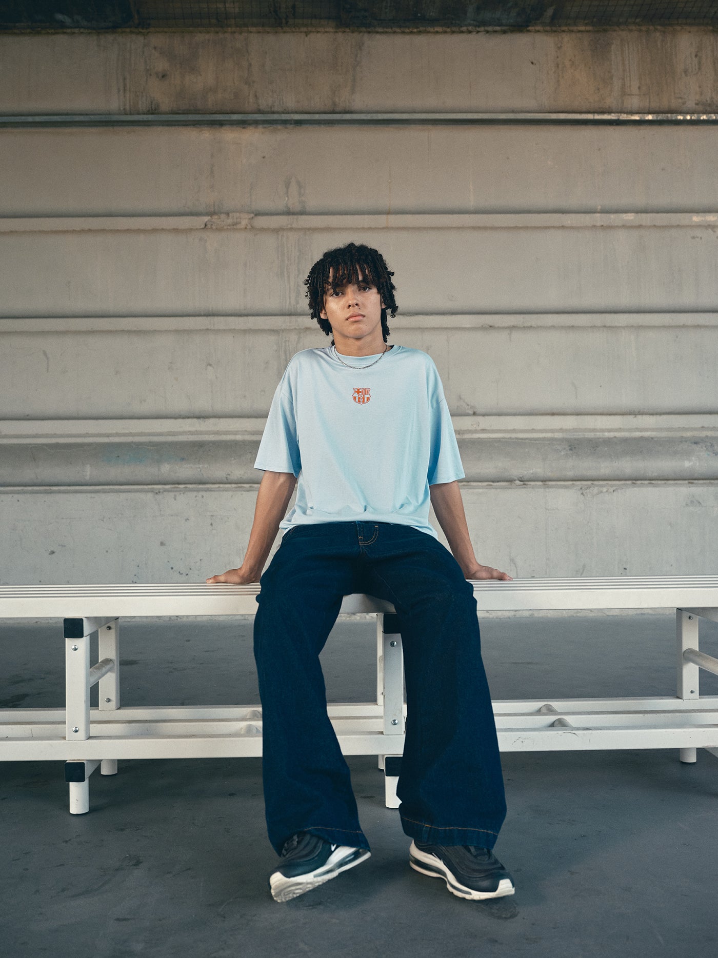 light blue FC Barcelona t-shirt with a large orange 'FCB' graphic and a black line illustration of a footballer kicking a ball