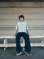 light blue FC Barcelona t-shirt with a large orange 'FCB' graphic and a black line illustration of a footballer kicking a ball