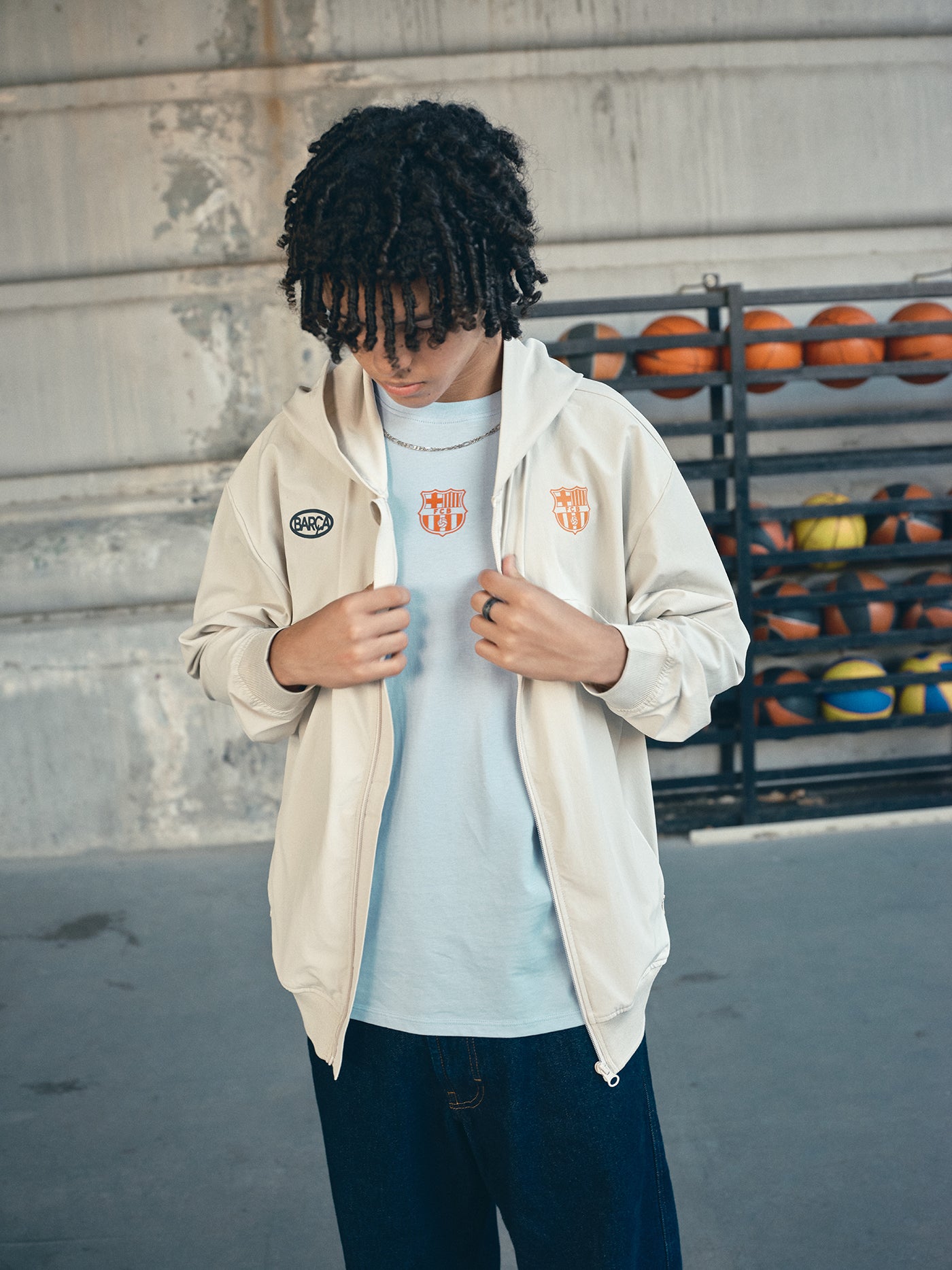 Beige FC Barcelona hooded jacket with minimalist orange graphic icons and text printed across the upper back.