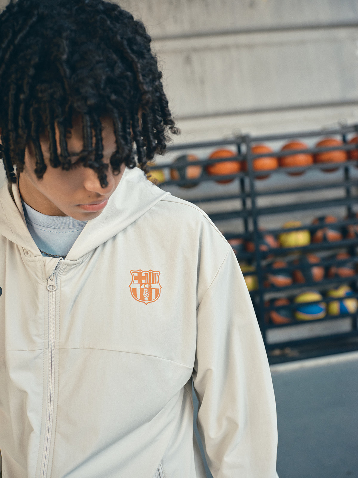 Beige FC Barcelona hooded jacket with minimalist orange graphic icons and text printed across the upper back.