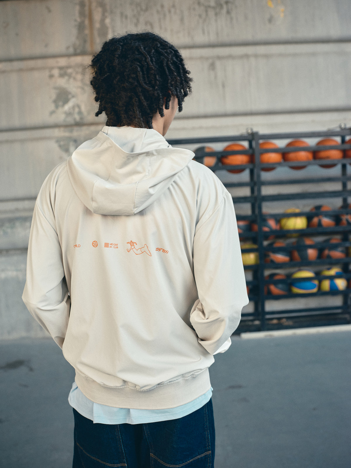 Beige FC Barcelona hooded jacket with minimalist orange graphic icons and text printed across the upper back.