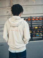 Beige FC Barcelona hooded jacket with minimalist orange graphic icons and text printed across the upper back.
