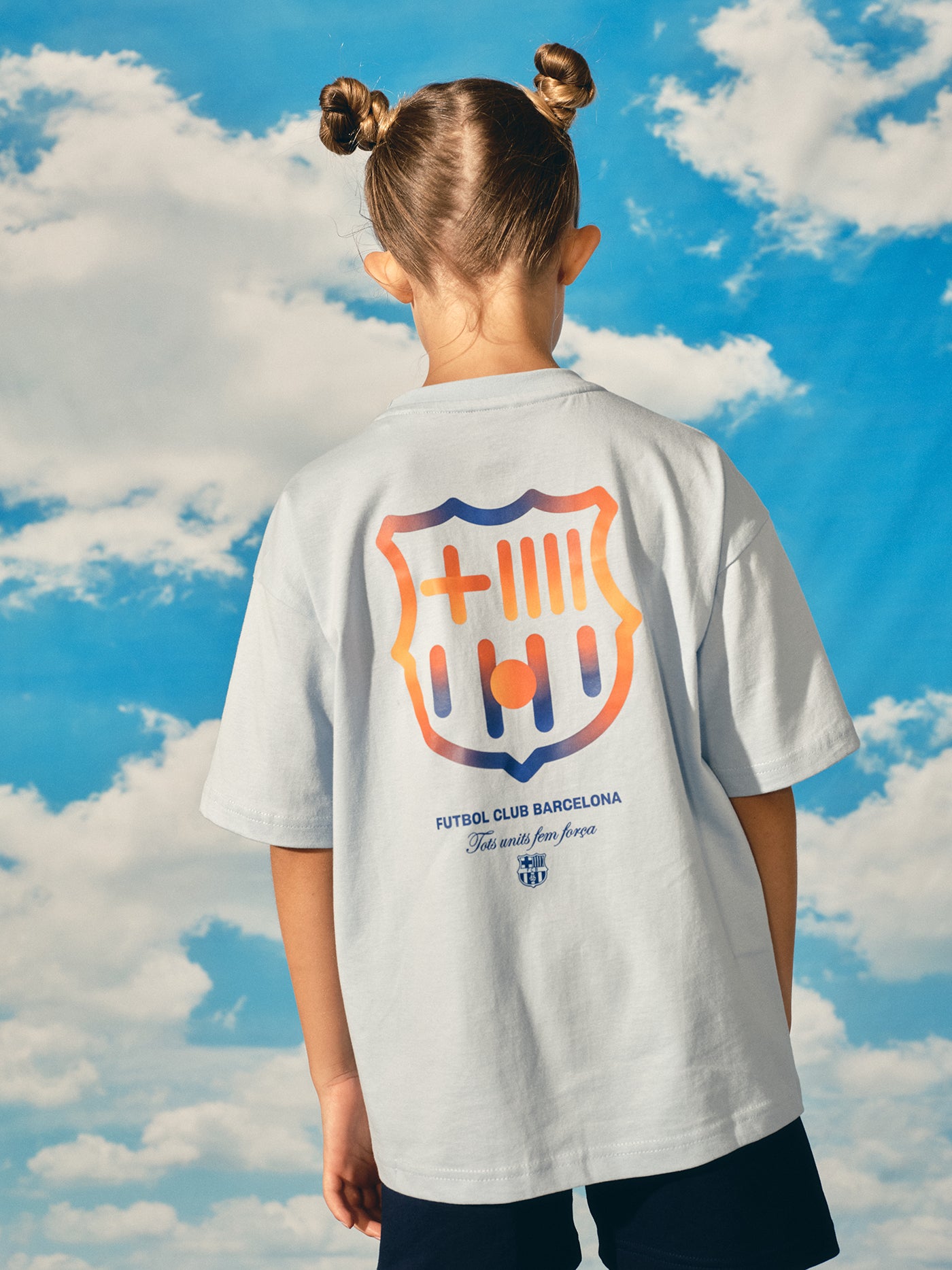 light grey FC Barcelona t-shirt with a large gradient club crest printed on the back, along with the text "Futbol Club Barcelona" and the motto "Tots units fem força