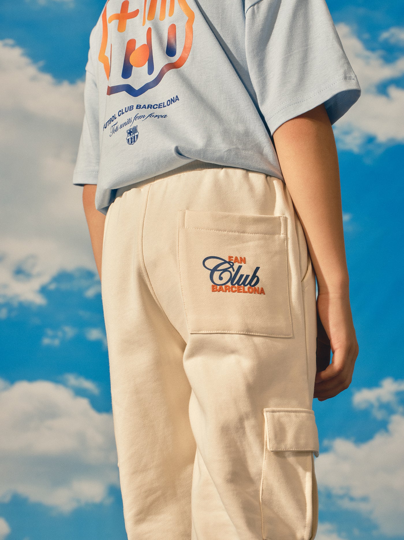 Beige FC Barcelona kids' jogger pants with side cargo pockets, elastic cuffs, drawstring waist, and club crest on the upper leg.