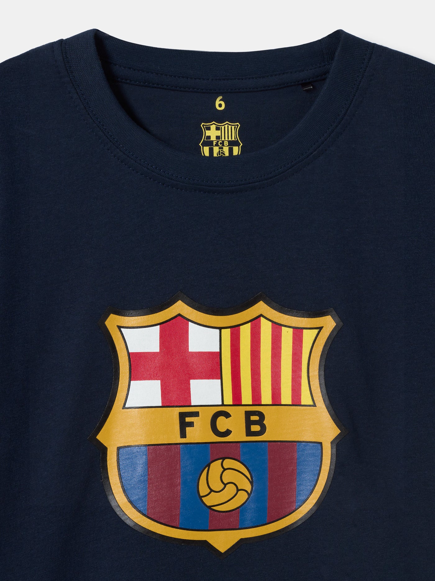 Back view of a navy blue FC Barcelona t-shirt featuring the phrase "MÉS QUE UN CLUB" in large, dark typography. Surrounding the text are red player autographs and jersey numbers, along with four yellow and red vertical bars representing the Catalan flag (senyera) near the neck.
