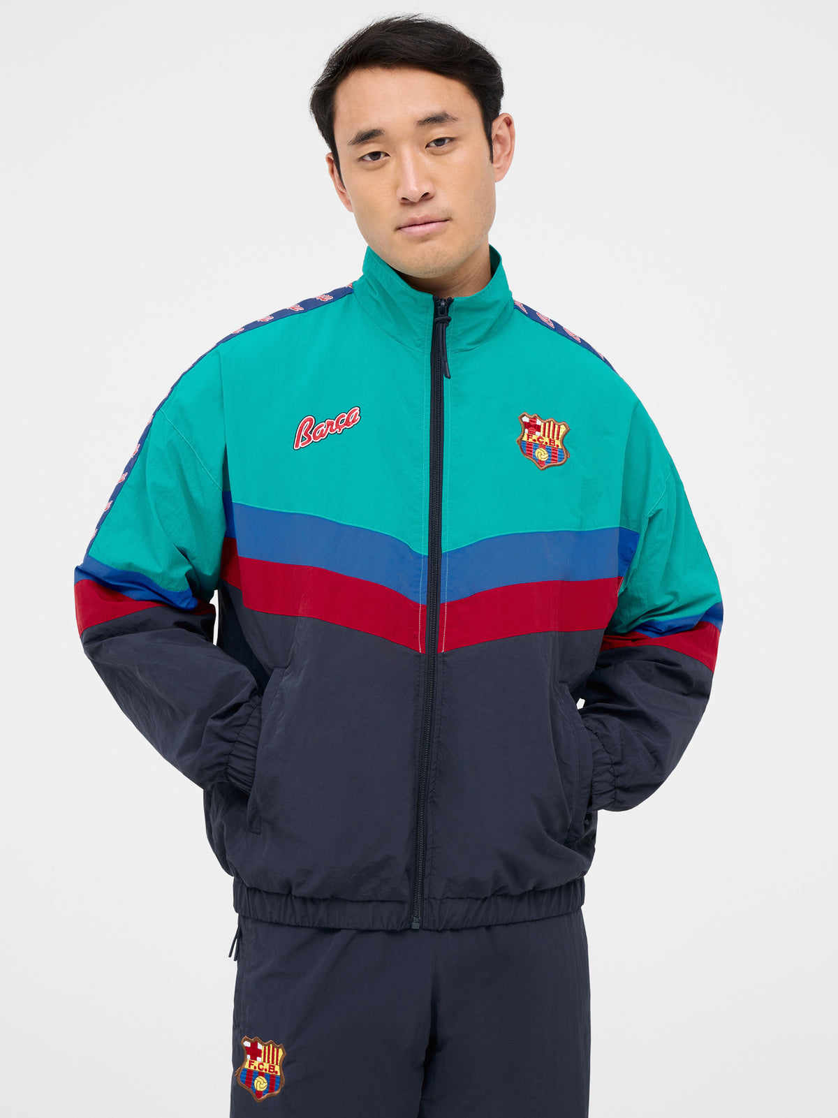 Retro-style windbreaker in teal, red, blue, and navy with FC Barcelona crest and embroidered 'Barça' text on the chest.