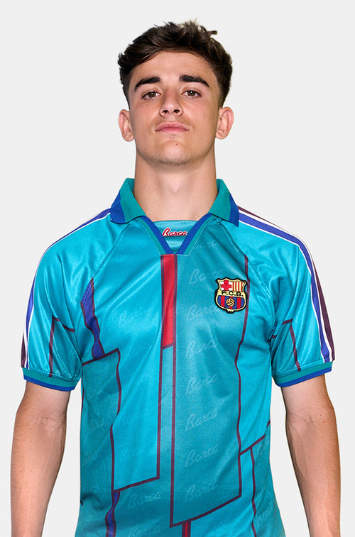Front view of a turquoise FC Barcelona shirt with dark blue and maroon graphic lines and the club crest on the chest.