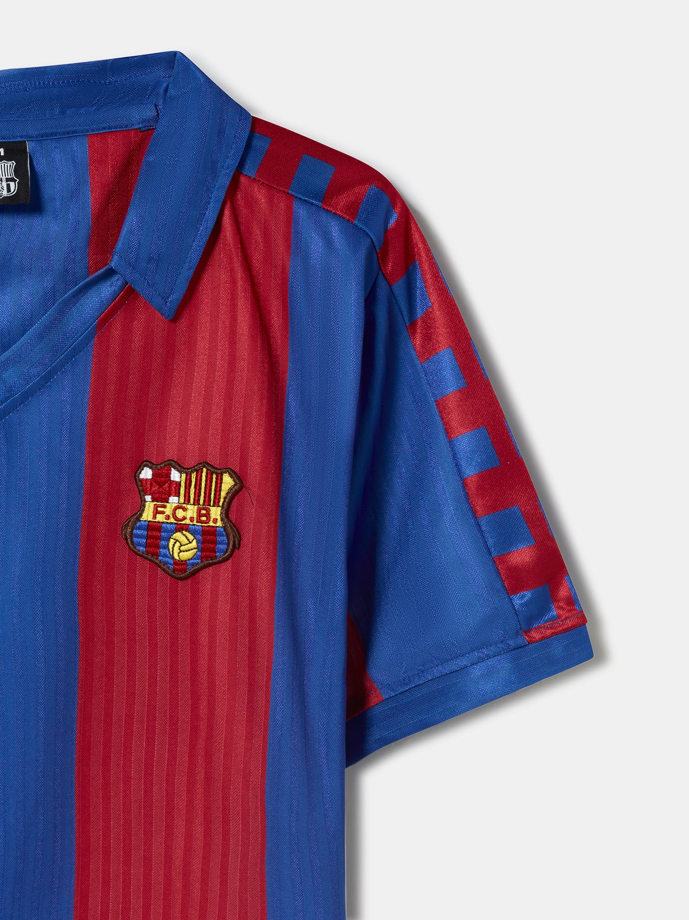Man wearing a retro-style FC Barcelona jersey with wide vertical red and blue stripes, featuring the club's crest on the left chest and a classic V-neck collar design.