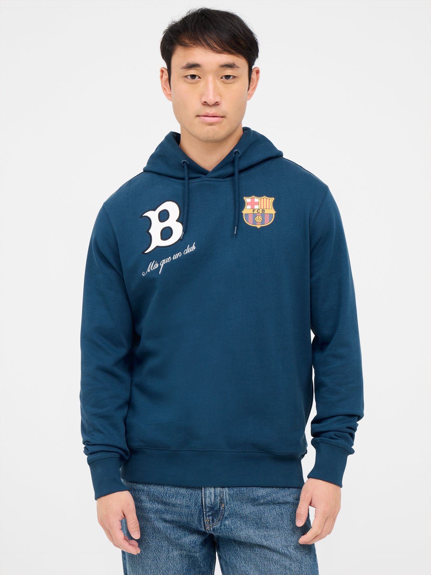 Man wearing a blue FC Barcelona hoodie, sitting with hands clasped. The hoodie features a white “B” on the left side with the phrase “Més que un club” below it, and the official FC Barcelona crest on the right side.
