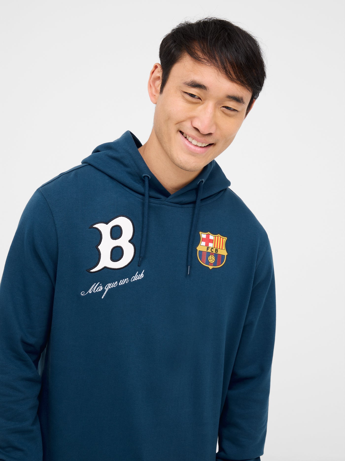 Man wearing a blue FC Barcelona hoodie, sitting with hands clasped. The hoodie features a white “B” on the left side with the phrase “Més que un club” below it, and the official FC Barcelona crest on the right side.









