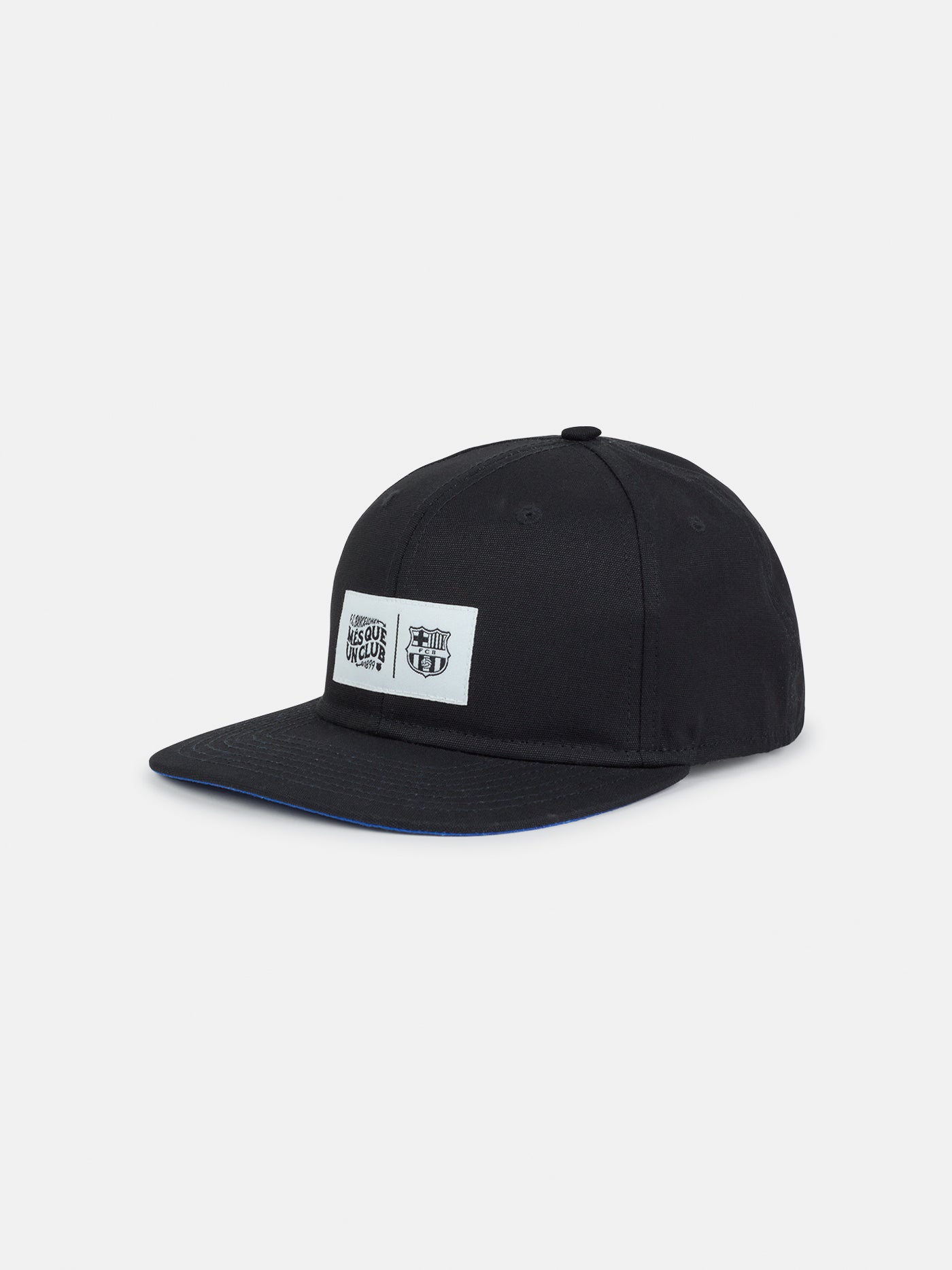 Black flat-brim cap featuring a rectangular white patch on the front with the FC Barcelona crest and the slogan "Més que un club" printed in black.