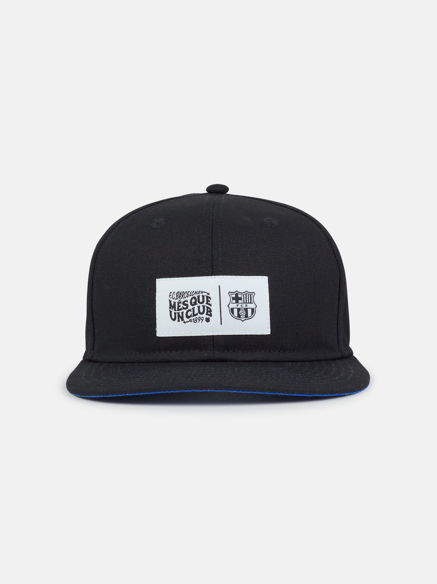 Black flat-brim cap featuring a rectangular white patch on the front with the FC Barcelona crest and the slogan "Més que un club" printed in black.