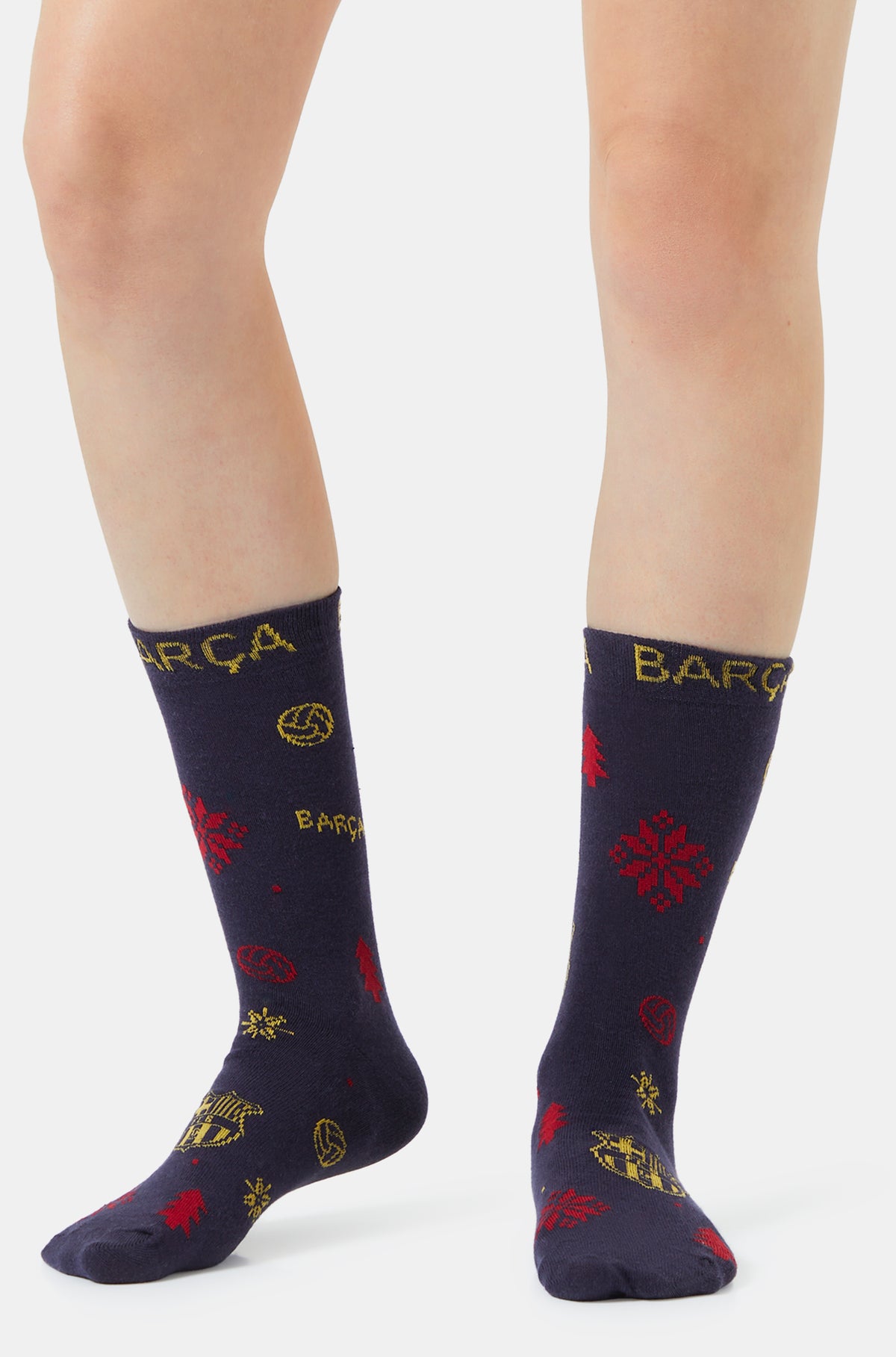 Pair of navy FC Barcelona socks with yellow Barça lettering and red winter-themed patterns, shown on a model’s lower legs.