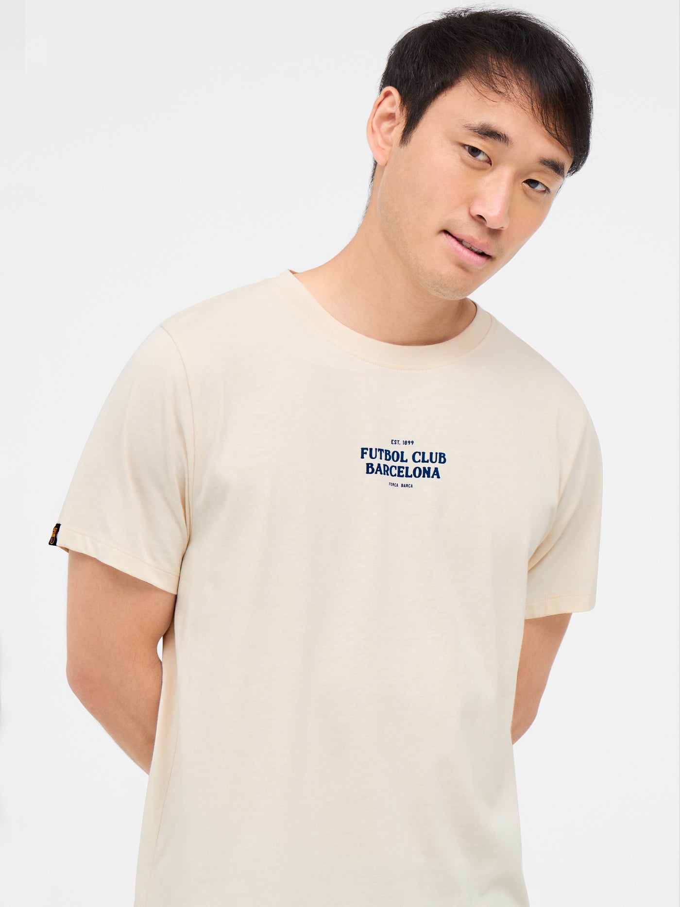  off-white FC Barcelona t-shirt with a red artistic illustration on the back, featuring iconic landmarks of Barcelona and the Camp Nou stadium inside a stylized club crest.