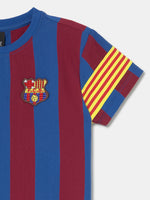 FC Barcelona kids’ T-shirt with blue and maroon vertical stripes, embroidered club crest on the chest, and yellow-red striped armband detail on the sleeve