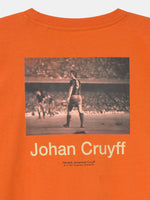 Bright orange T-shirt featuring a black-and-white image of Johan Cruyff during a match and his name below the photo