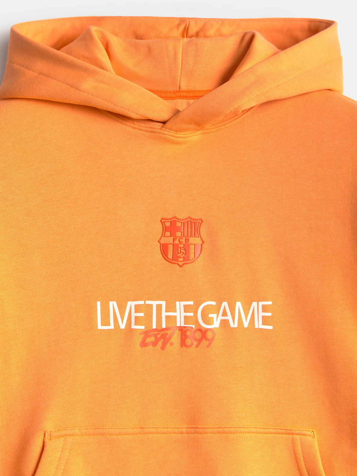Vista frontal de una sudadera con capucha naranja de FC Barcelona con el escudo del club y el texto “LIVE THE GAME” en el pecho.