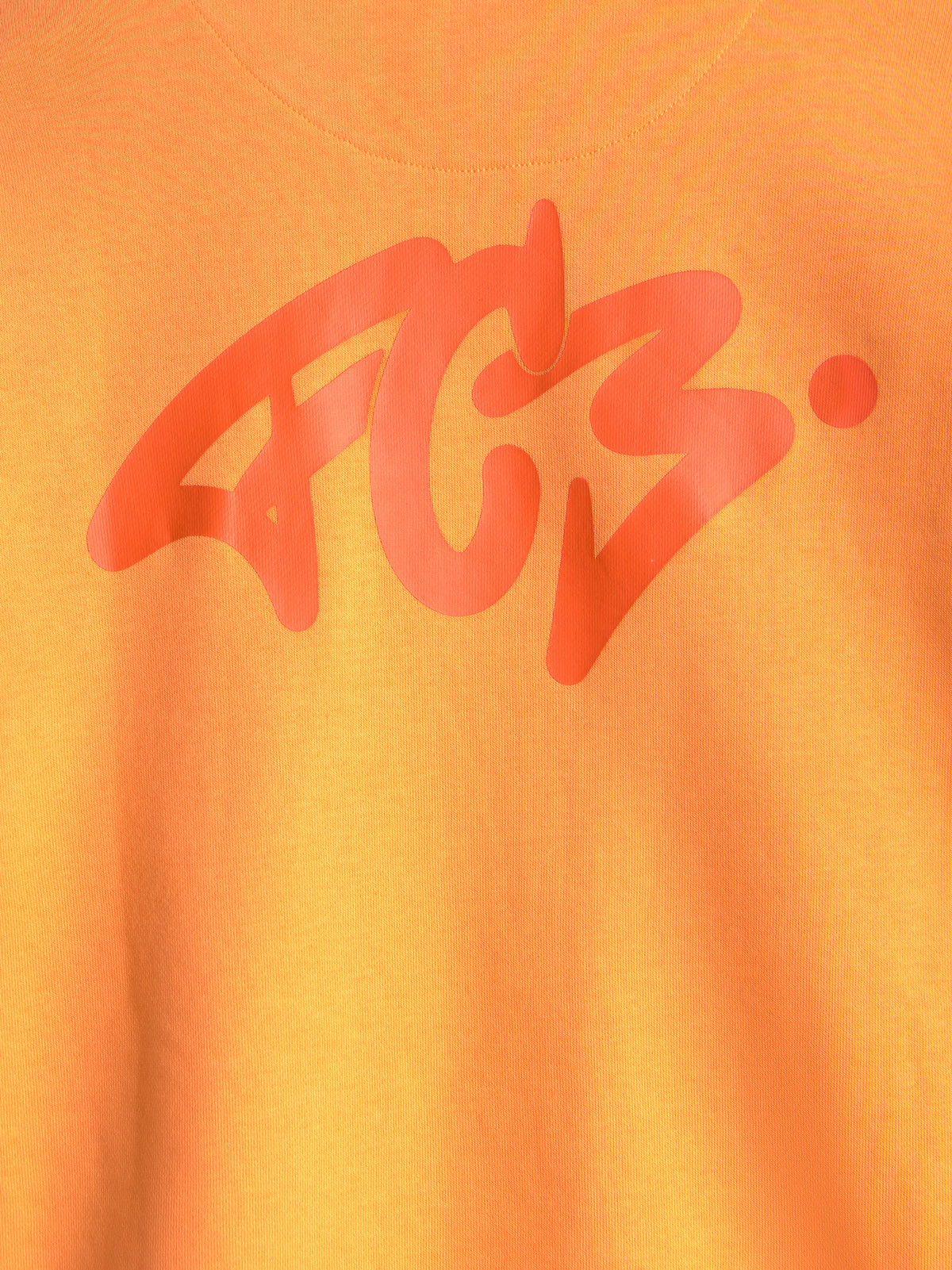 Primer plano de una camiseta naranja del FC Barcelona con un gran gráfico abstracto rojo estampado en el pecho.