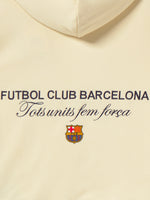 Beige FC Barcelona hoodie for kids, featuring a colorful 'Barça' text on the front and 'Futbol Club Barcelona - Tots units fem força' with the club crest on the back