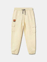 Beige FC Barcelona kids' jogger pants with side cargo pockets, elastic cuffs, drawstring waist, and club crest on the upper leg.