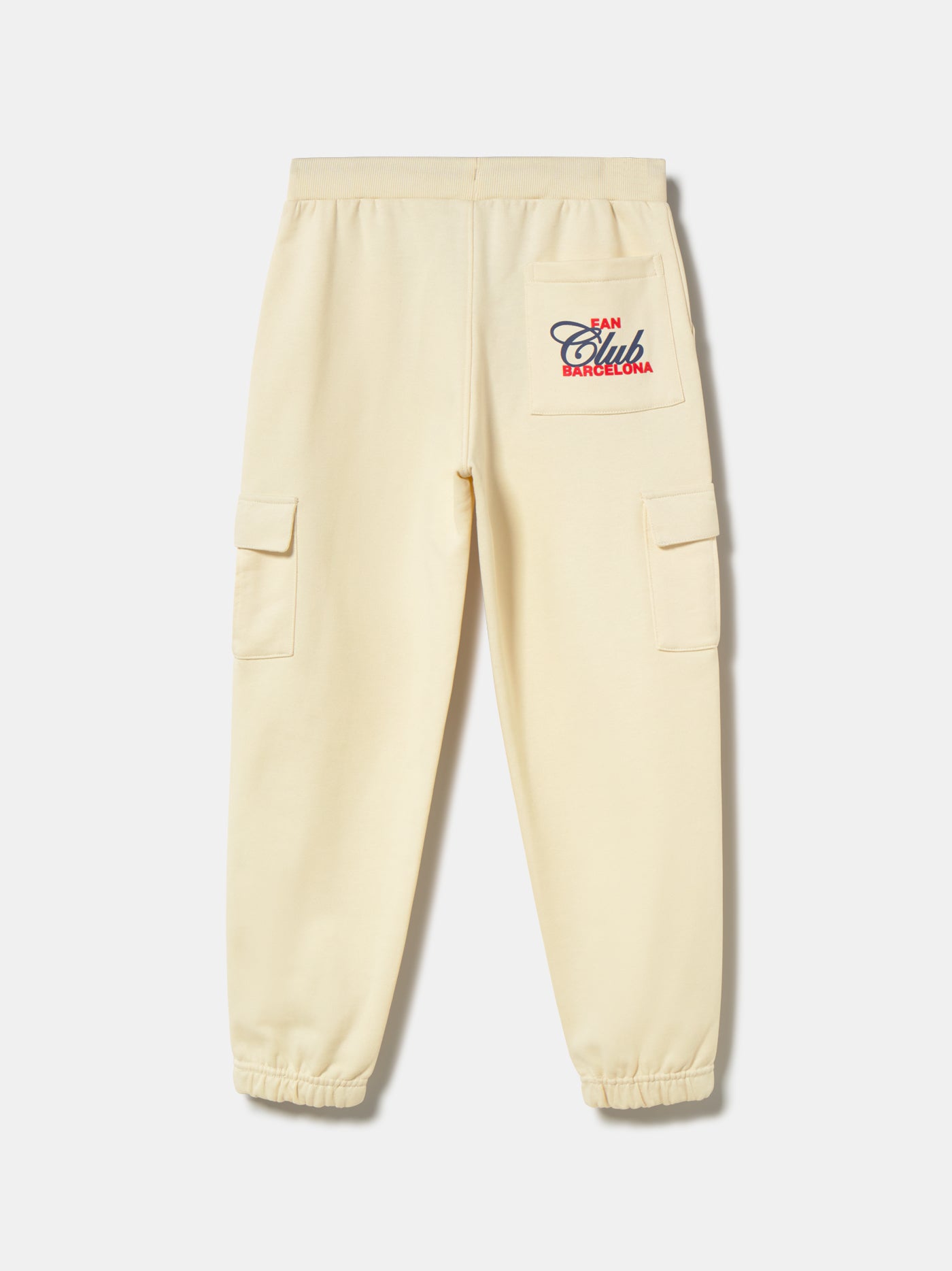 Beige FC Barcelona kids' jogger pants with side cargo pockets, elastic cuffs, drawstring waist, and club crest on the upper leg.