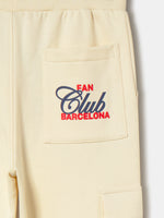Beige FC Barcelona kids' jogger pants with side cargo pockets, elastic cuffs, drawstring waist, and club crest on the upper leg.