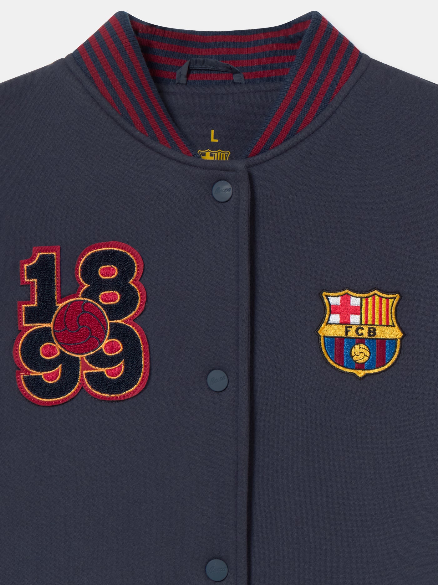 Navy blue FC Barcelona varsity jacket with embroidered 1899 detail, club crest on the chest, and red striped collar, cuffs, and hem.