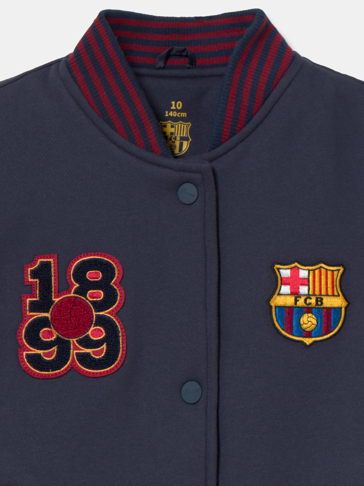 Navy blue FC Barcelona varsity jacket with embroidered 1899 detail, club crest on the chest, and red striped collar, cuffs, and hem.