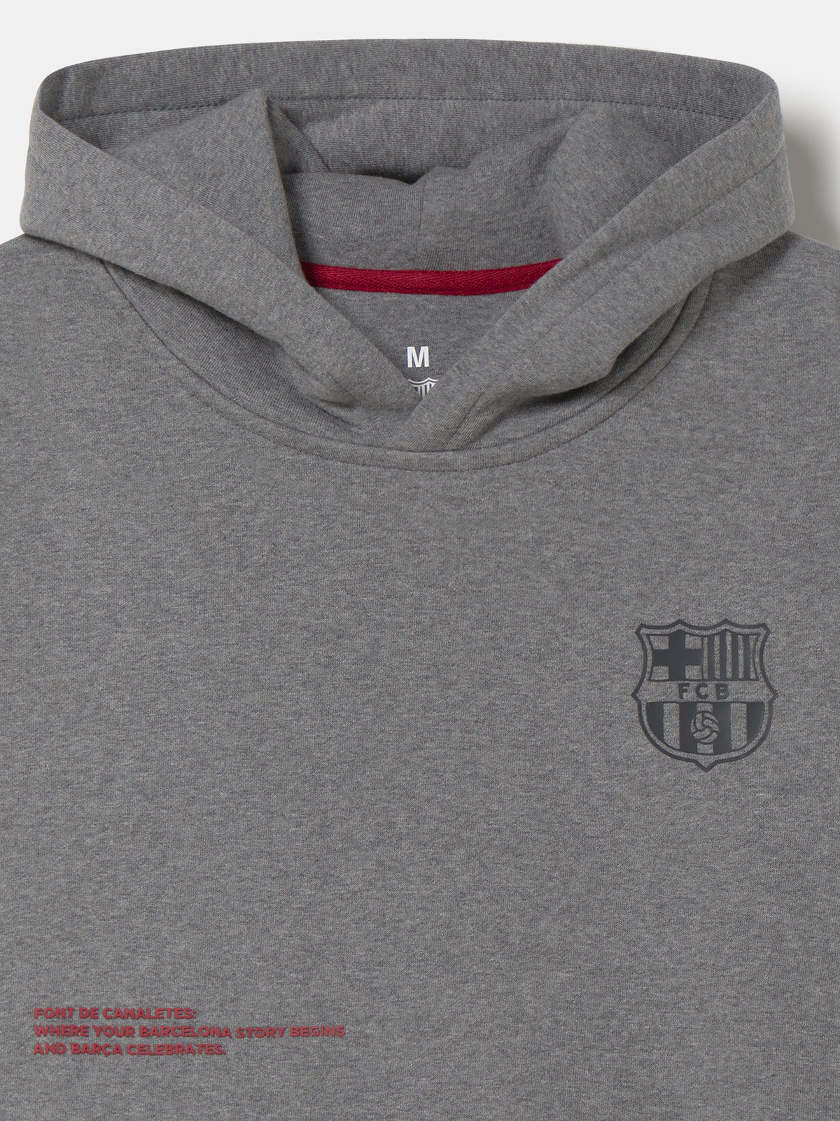 Front view of a grey FC Barcelona hoodie with a cowl-style hood, dark Barça crest on the chest, and small red text near the hem.