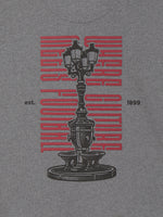 Heather gray T-shirt with a large black vintage streetlamp graphic, red vertical lettering, and small “est. 1899” text on the front.