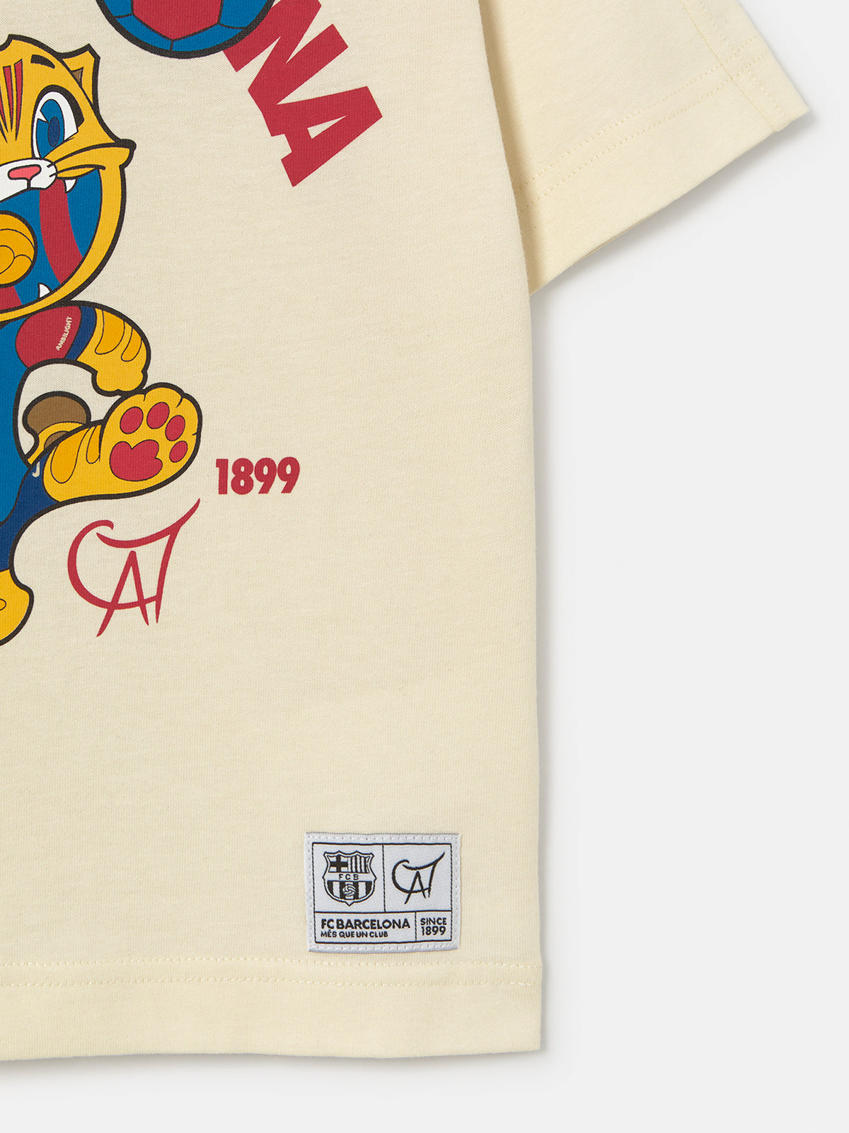 cream FC Barcelona T-shirt featuring the club's name and Cat Culer, the cartoon mascot, playing football.