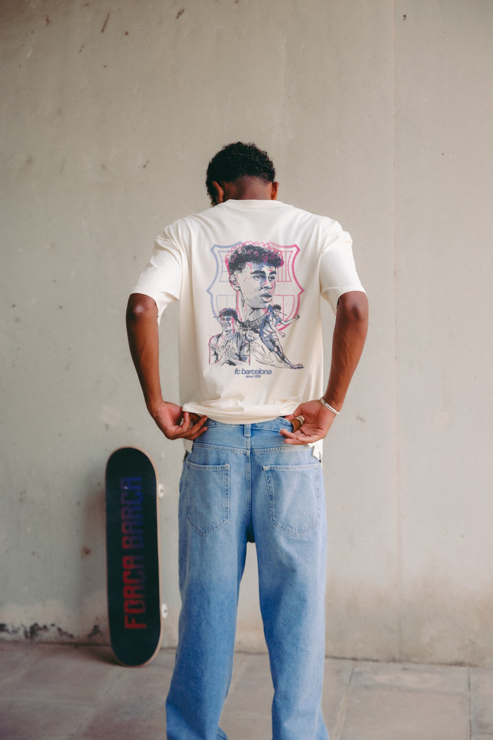 Off-white T-shirt featuring an illustrated graphic of Lamine Yamal with FC Barcelona elements and 'fc barcelona' text on the back.