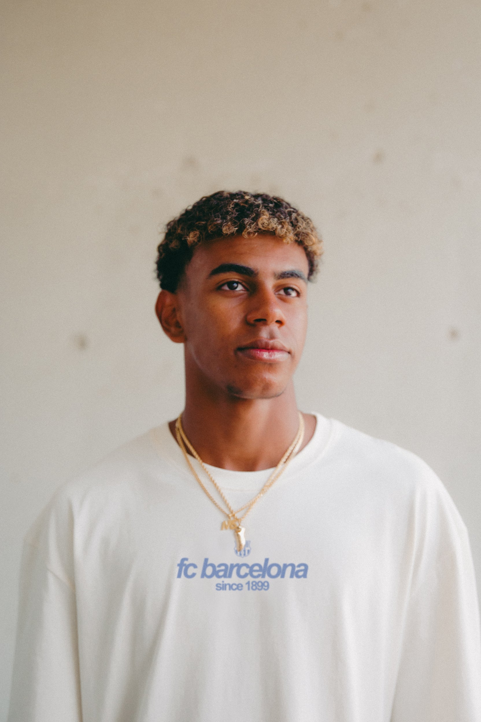 Off-white T-shirt featuring an illustrated graphic of Lamine Yamal with FC Barcelona elements and 'fc barcelona' text on the back.