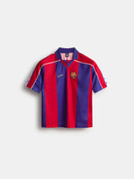 Vista frontal de una camiseta a rayas del FC Barcelona con cuello marino, paneles verticales rojos y azules, ribete blanco en los hombros y el escudo del club en el pecho.