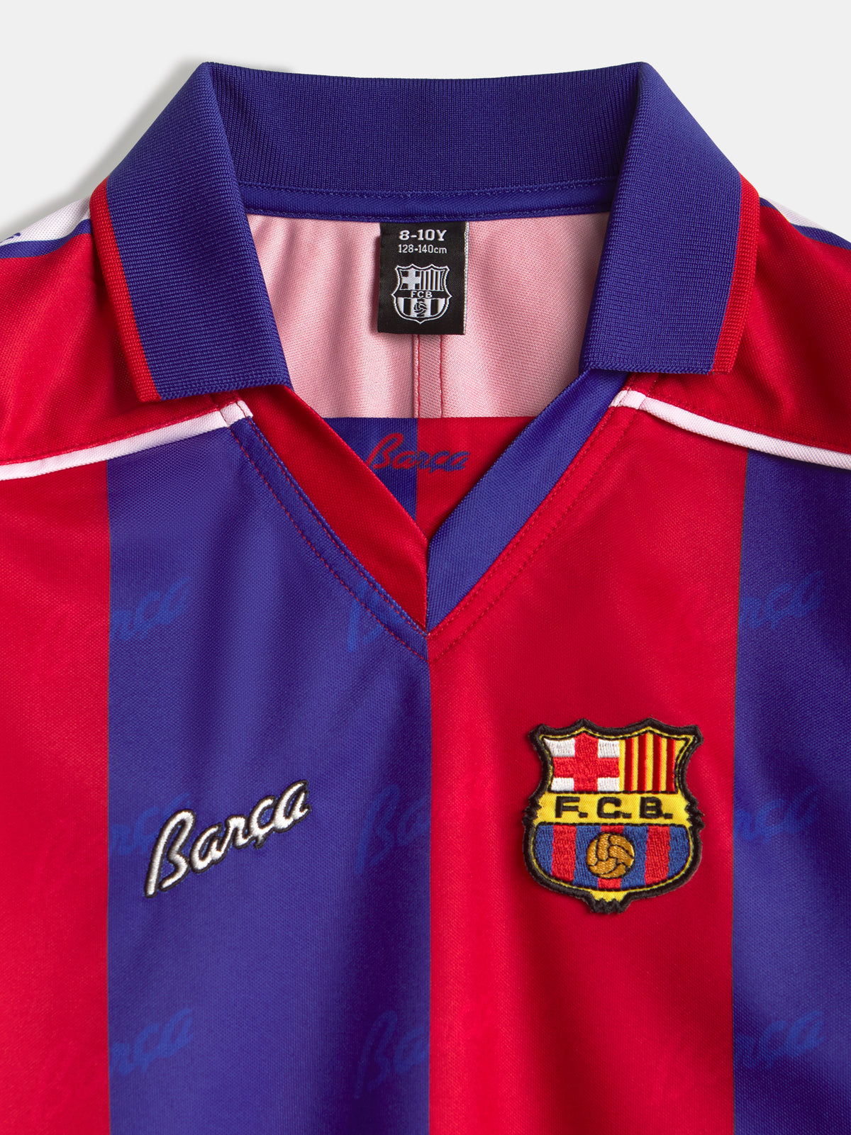 Vista frontal de una camiseta del FC Barcelona con franjas verticales rojas y azules, cuello morado y el escudo del club en el pecho.