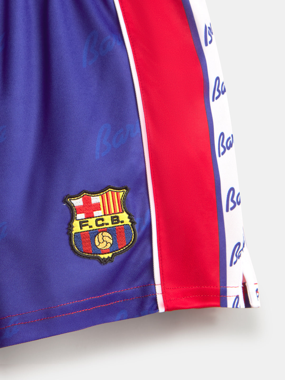 Détail de l'écusson du FC Barcelona sur un tissu bleu avec une bande latérale rouge et blanche.
