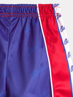 Gros plan sur un short FC Barcelona à base violette, panneau latéral rouge et bordure blanche avec imprimé répété du logo Barça.