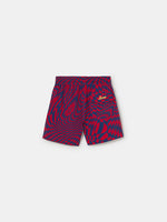 FC Barcelona swim shorts with a bold red and blue optical illusion checkerboard pattern, featuring an elastic waistband with drawstring and a yellow patch logo near the hem.